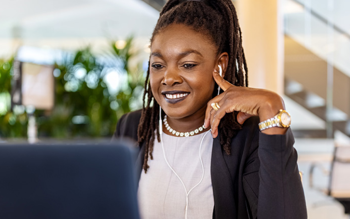 A woman sits at a desk wearing headphones while listening to a video call