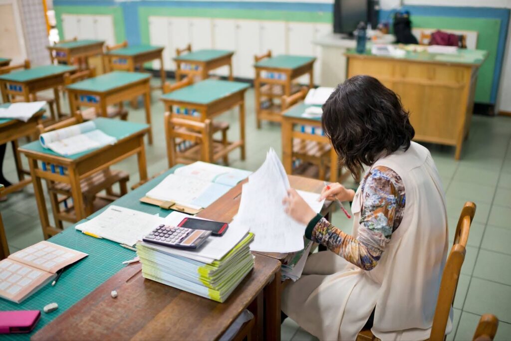 A teacher grades assignments at her desk in an otherwise empty classroom.