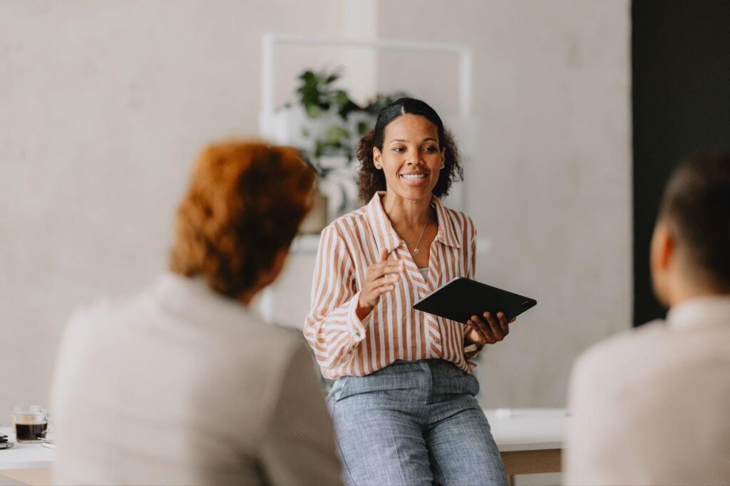 A confident businesswoman leads a group business meeting in an office meeting space.